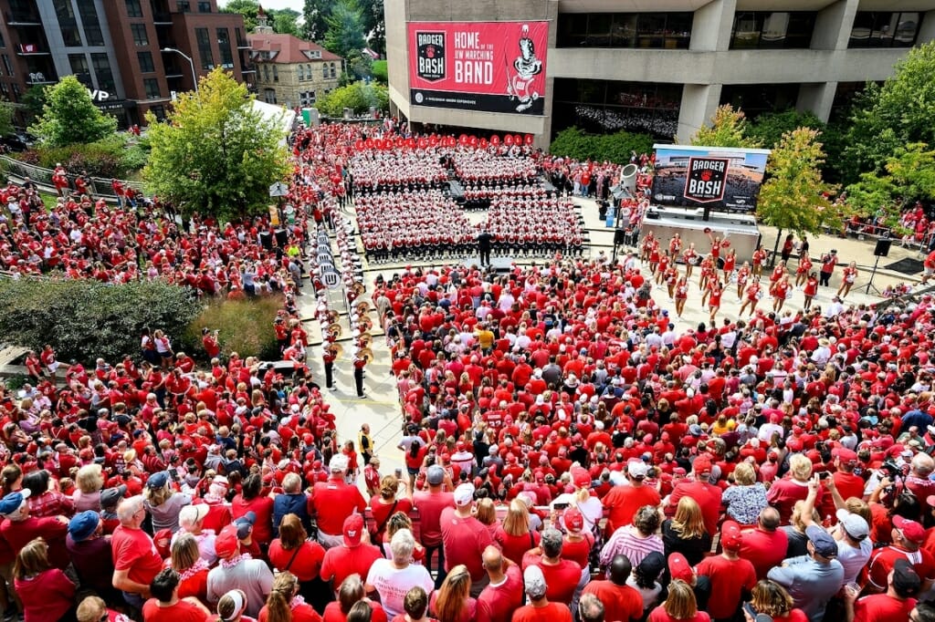 Photo: Wide shot of people, mostly wearing red, listening to band and watching cheerleaders