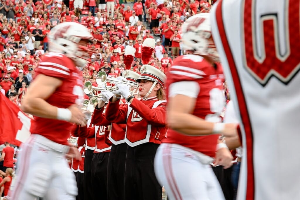 Photo: Uniformed players passing uniformed band members playing horns