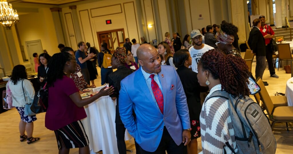 Photo: A man in a blue suit speaks to others at a reception.