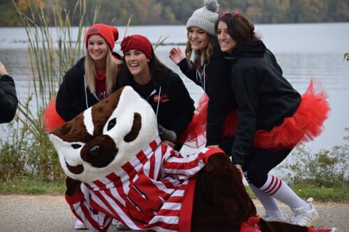 Students wearing athletic clothes and tutus pose with Bucky Badger.