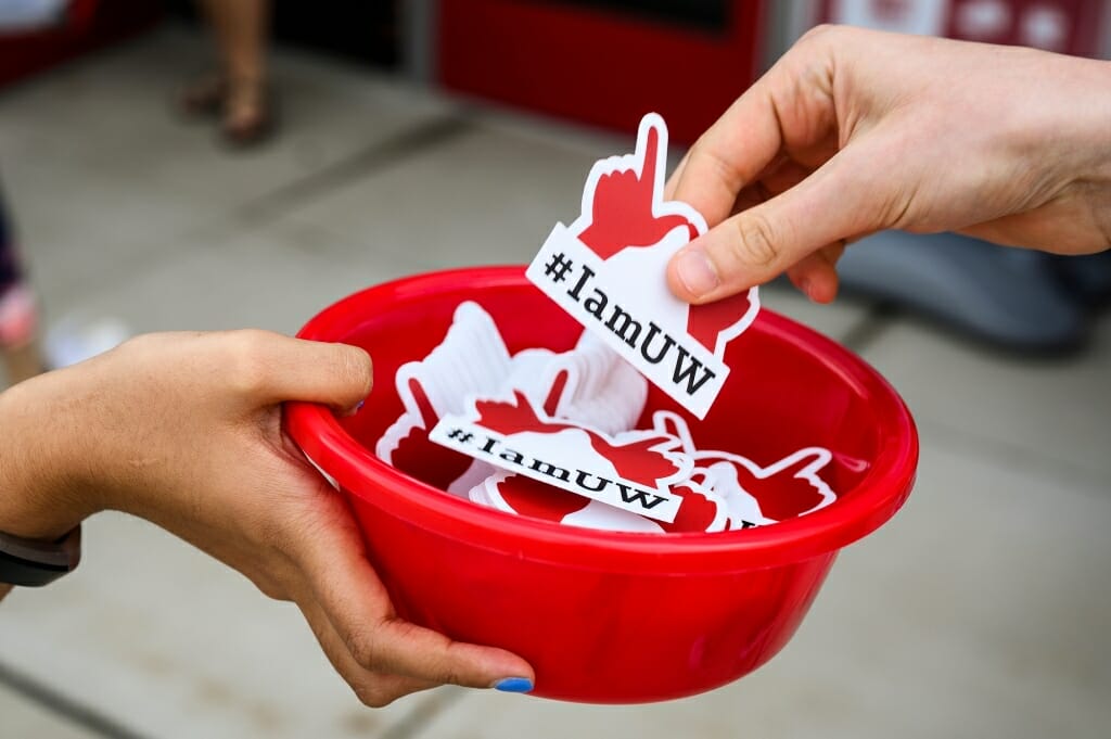 Photo: Closeup of person's hand holding bowl of stickers and another person taking one