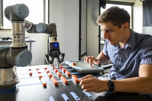 Photo: Andrew typing on a small screen in front of a robot arm