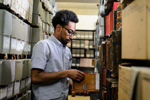 Photo: Long standing between library shelves paging through book