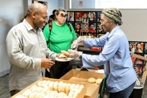 Photo: Person serving food next to a table full of sandwich rolls