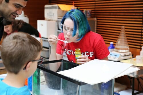 Photo: Person blowing a bubble as child and adult watch