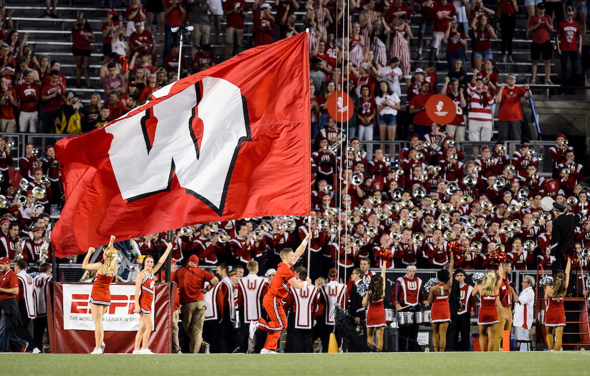 Photo of a cheerleader with the UW Spirit Squad running a large W flag across the field during a season-opening, night football game between the Wisconsin Badgers and the Western Kentucky Hilltoppers at Camp Randall Stadium at the University of Wisconsin–Madison on Aug. 31, 2018.