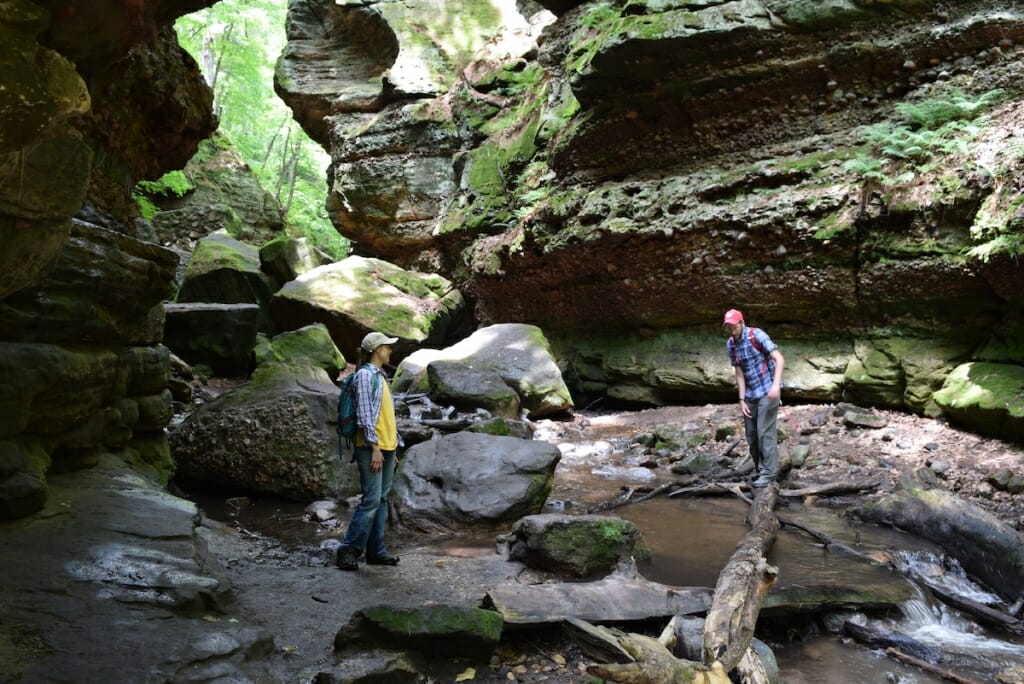 Two people walk through a mysterious rock formation formed by water.