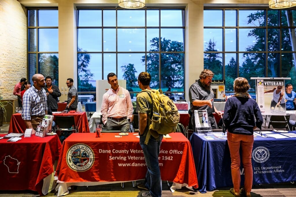 Photo: Student wearing backpack talking to man behind Dane County Veterans Service Office table