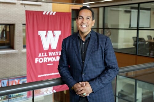 Photo: Portrait of Aaron Bird Bear standing in front of a "W All Ways Forward" banner