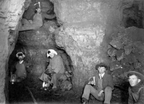 Black and white photo of a handful of miners sitting in a cave.