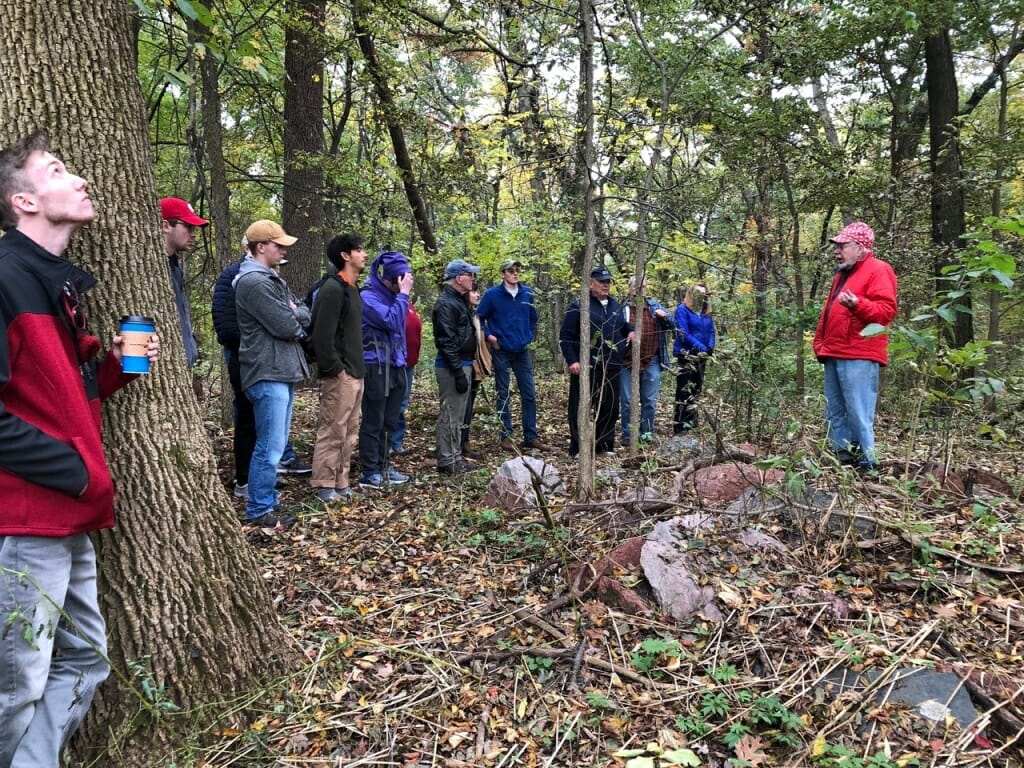 Photo: A man talks to a group of people in the woods.