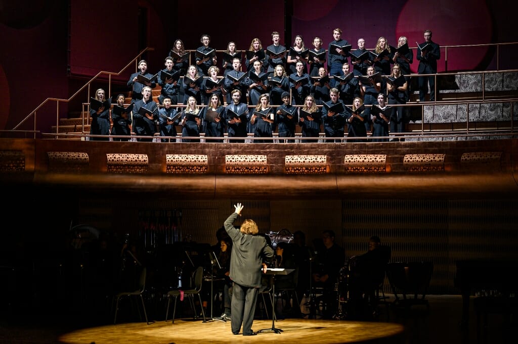 Photo: Conductor seen from behind with choir above on risers