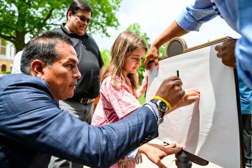 Photo: Bird Bear and child rubbing crayons on paper held against plaque