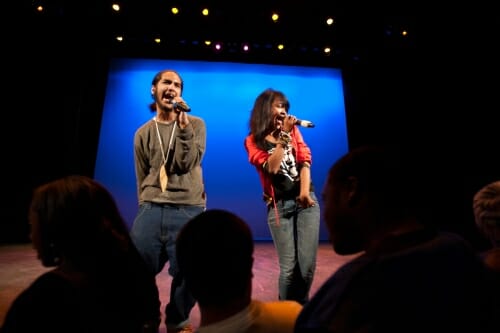 Photo: 2 people standing on a stage speaking into microphones