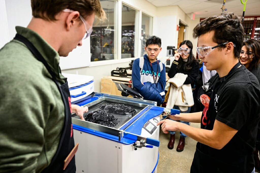 Makerspace staff Jake Rymsza, left, and Kirk Mendoza operate a thermoforming machine.