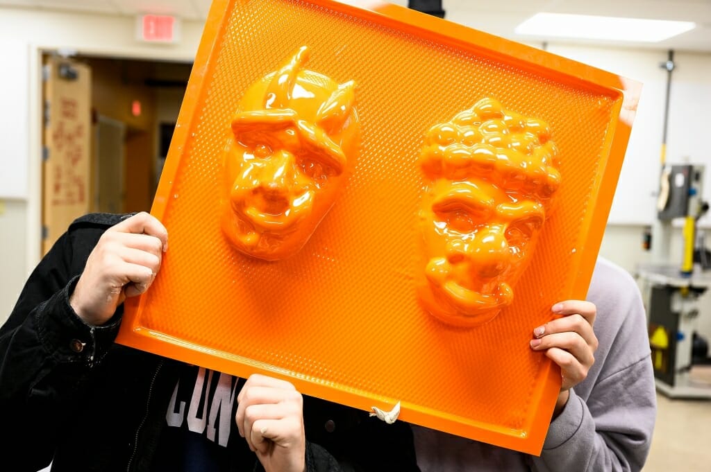 Photo: Person's hands holding up orange mold with 2 masks on it