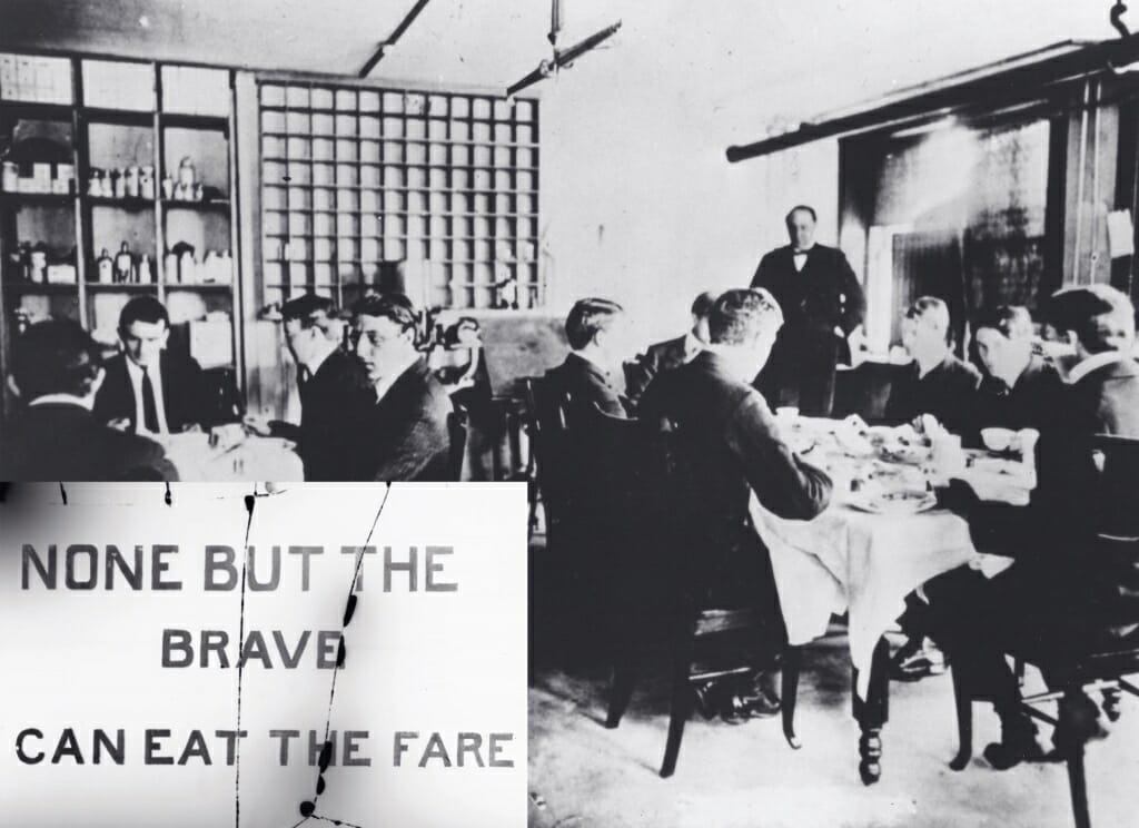 Photo: Men sitting around dining tables behind a sign that says "None but the brave can eat the fare"