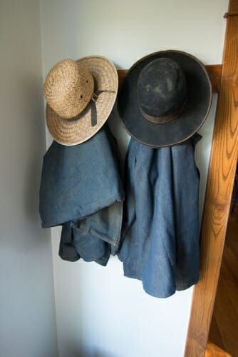 A pair of coats and hats hang on a wooden hook.