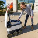 Photo: A woman takes her order out of a food delivery robot.