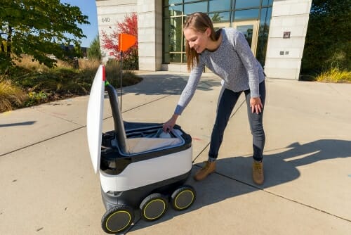 Photo: A woman takes her order out of a food delivery robot.