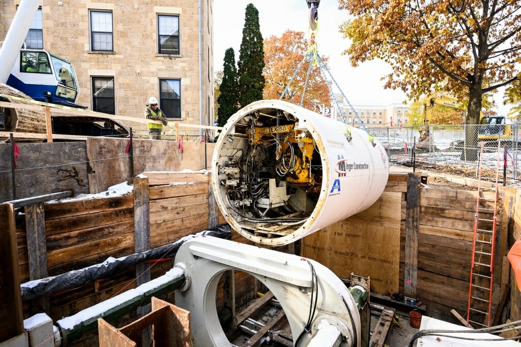 The bore head is lowered down into the reinforced earthen pit between South Hall and the Law Building.