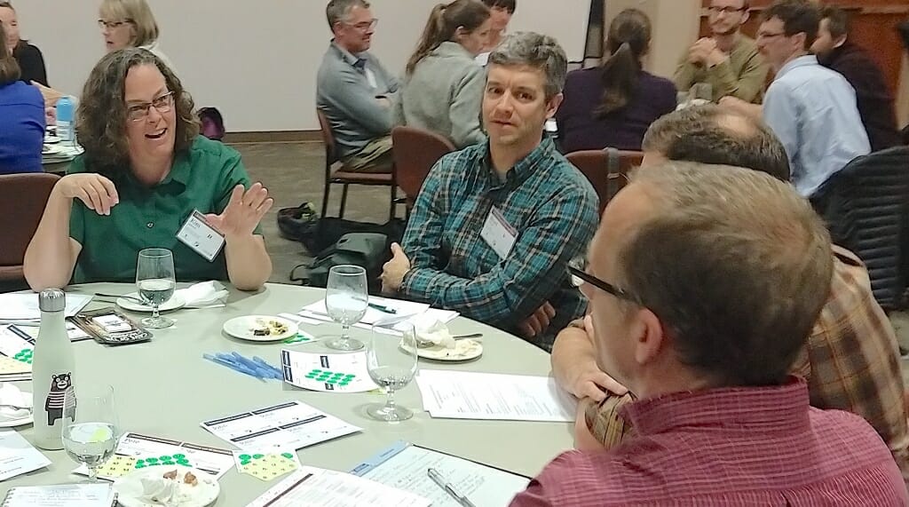 Photo: Kim Anderson and Brad Herrick sitting at a table talking to unidentified people