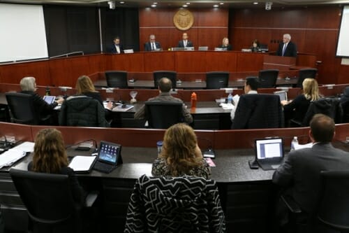 Council members sit on a dais in front of an audience.