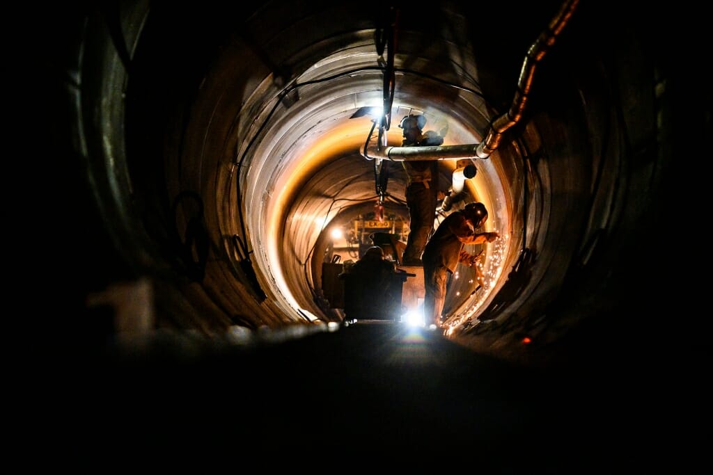 Photo: Workers weld and talk inside a darkened tunnel.