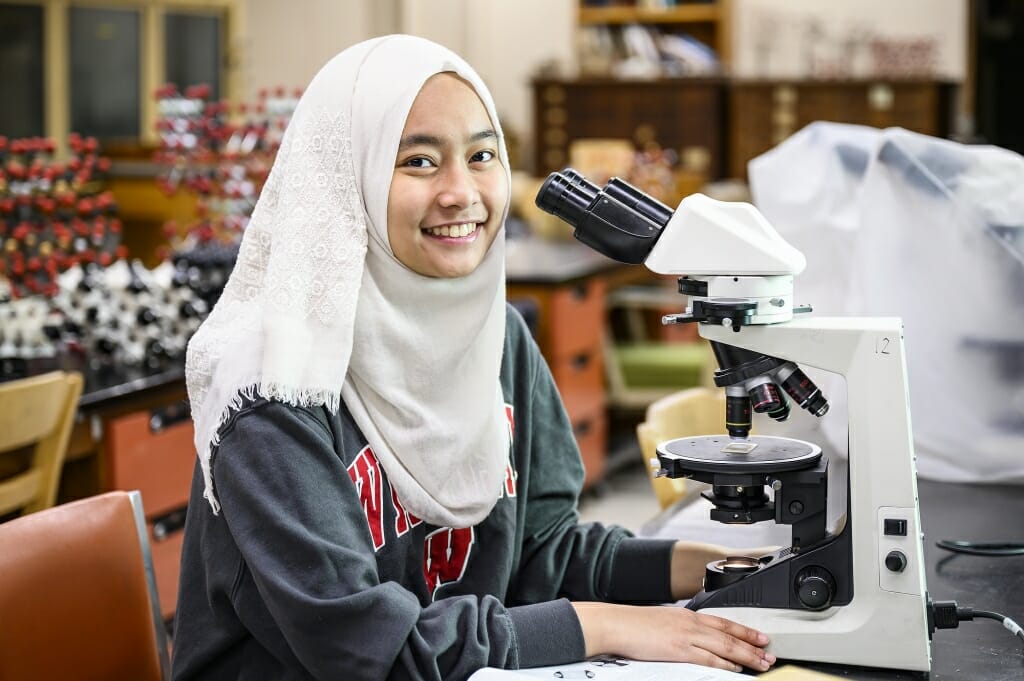 Photo: Lisa sitting next to a microscope