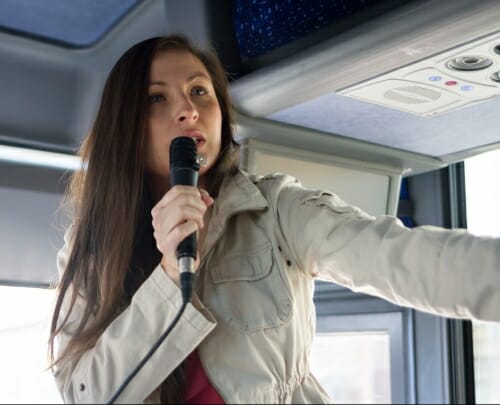 Photo: Melissa Metoxen standing inside a bus speaking into a microphone