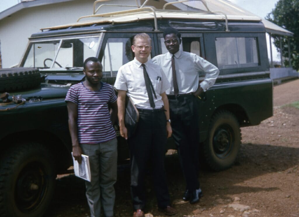 Photo: M. Crawford Young, Isaac Ojok and James Katorobo posing in front of a large Jeep-like vehicle