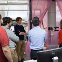 Photo: Students standing looking at computer behind pink curtain