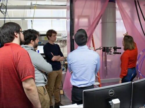 Photo: Students standing looking at computer behind pink curtain