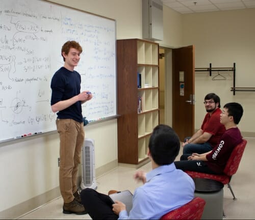 Photo: Student standing in front of whiteboard with equation on it