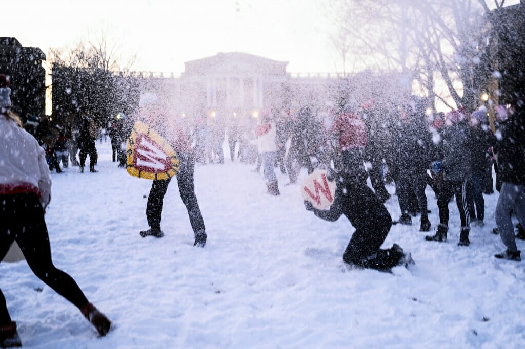 A person holding a W crest shield in front of Bascom Hall