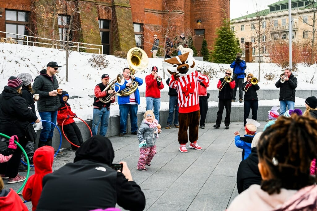 Bucky Badger dances with a child, with a band in the background.