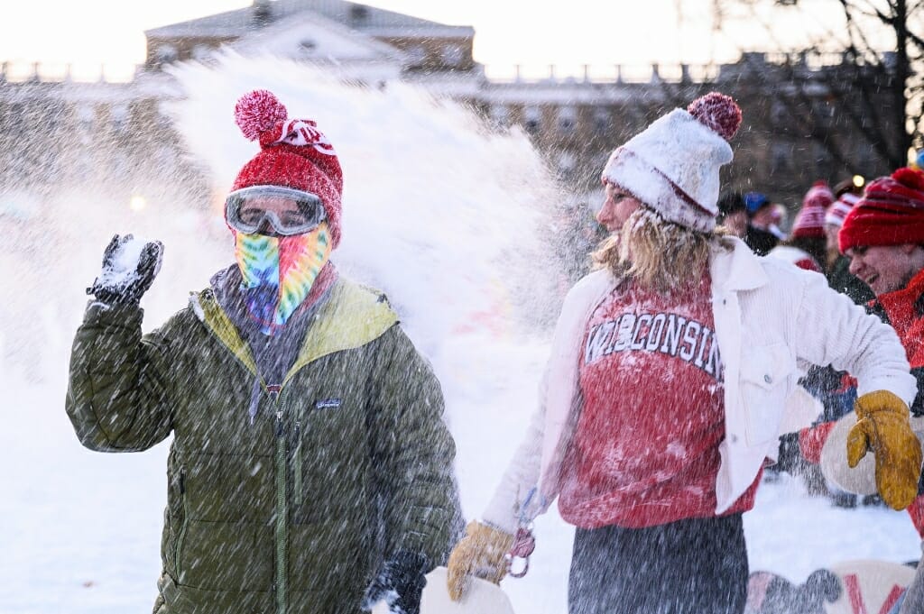 A person wearing ski goggles and a scarf, holding a snowball