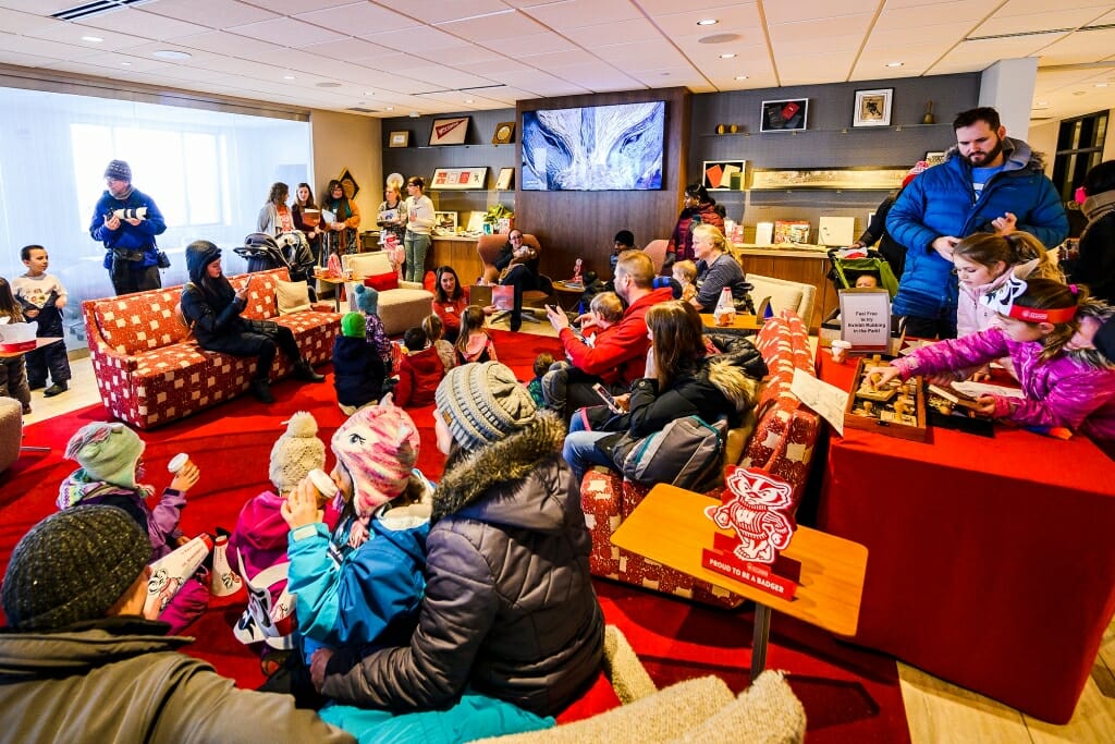 A crowded room at the Alumni Center, with a TV on and many sipping hot chocolate.