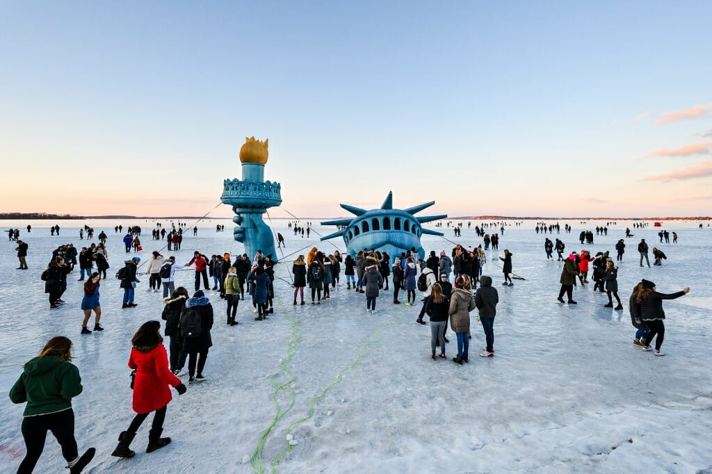 People flock around an inflatable Statue of Liberty head on the ice and take photos.