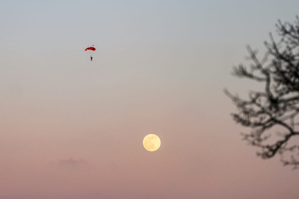 A sky diver floats by the moon.