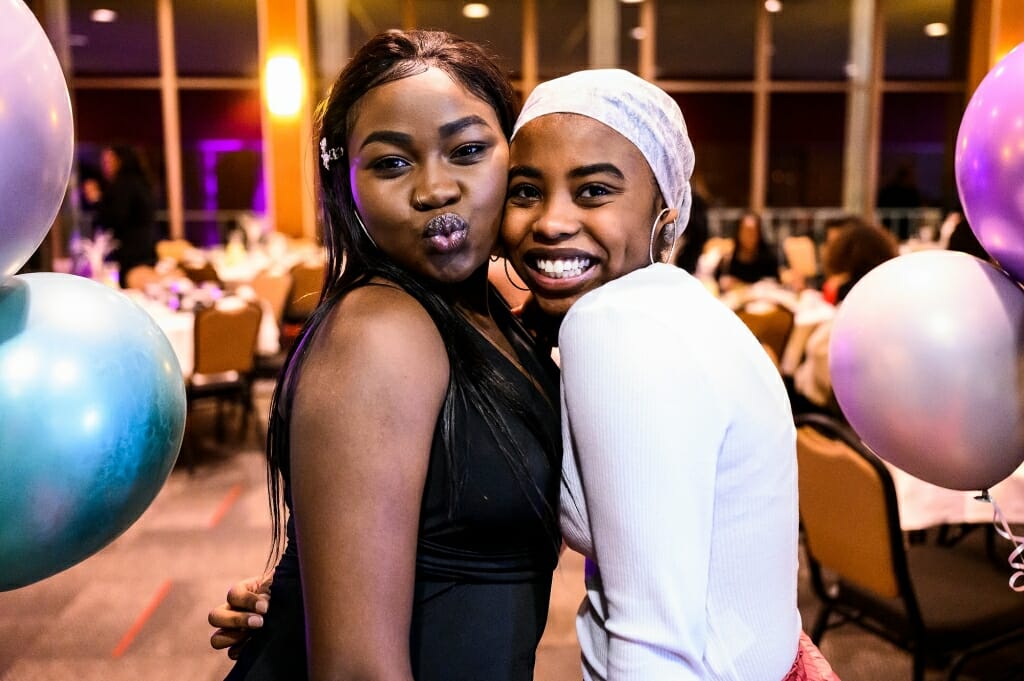 Two women stand close together and smile for the camera.