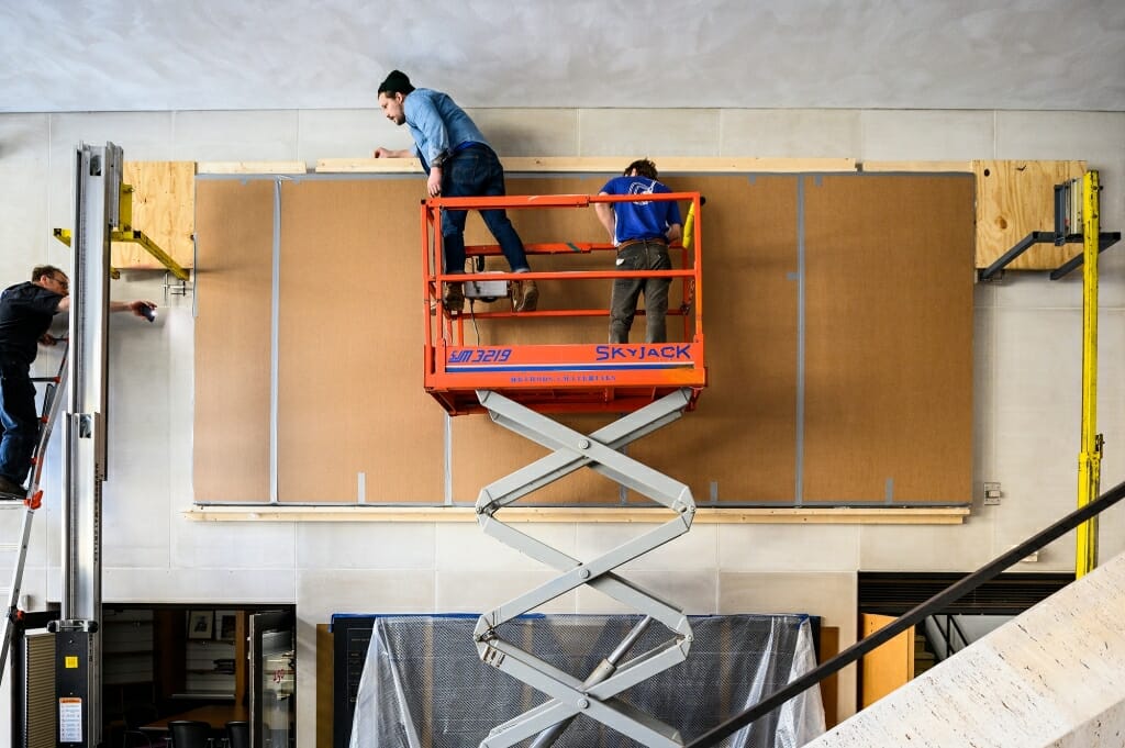 Workers on a scissors lift measure the mural.