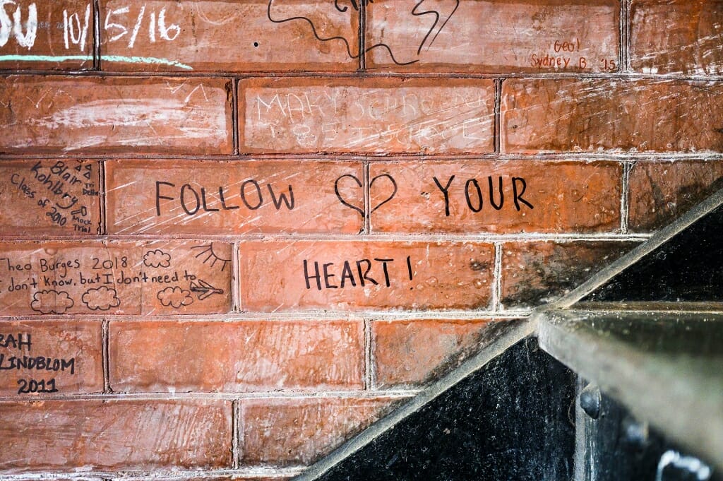 A brick wall has a heart sketched and the words 