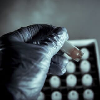 A hand holds a test tube above a rack of test tubes.