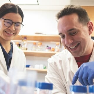 Two people in white lab coats work with test tubes.