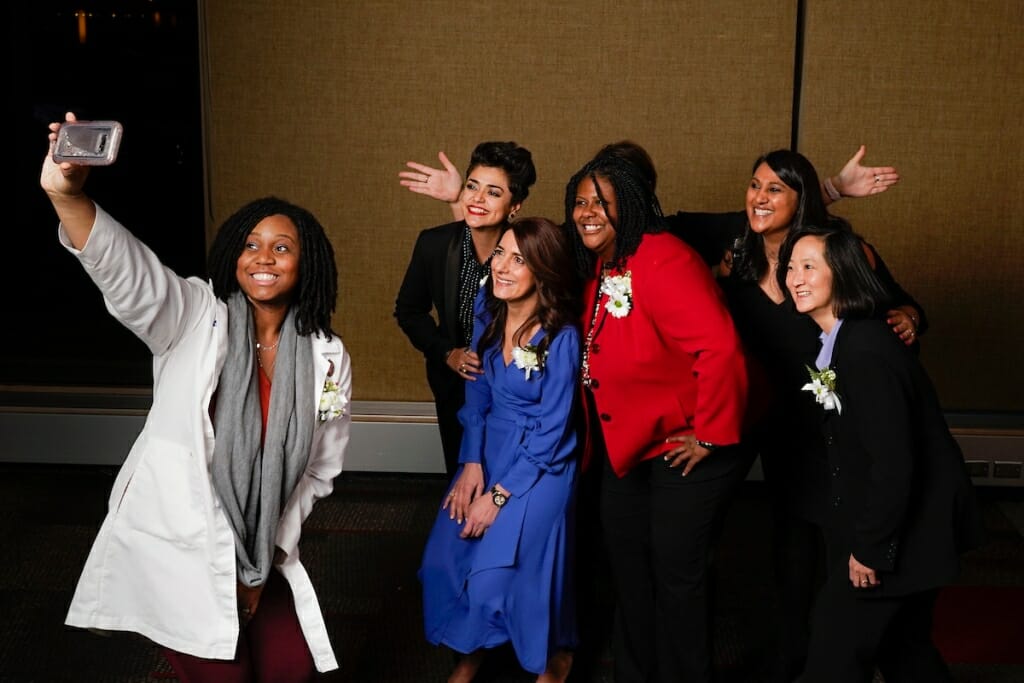 Seven women pose for one holding up a camera.