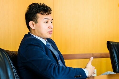 Lorenzo sitting at a table, gesturing with hand while speaking to interviewer (off camera)