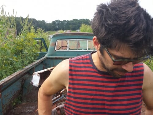 Pinc standing behind a green pickup truck, looking down through sunglasses