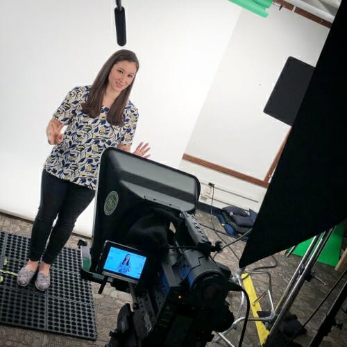 Lori Lopez standing in front of a white background, speaking into a video camera