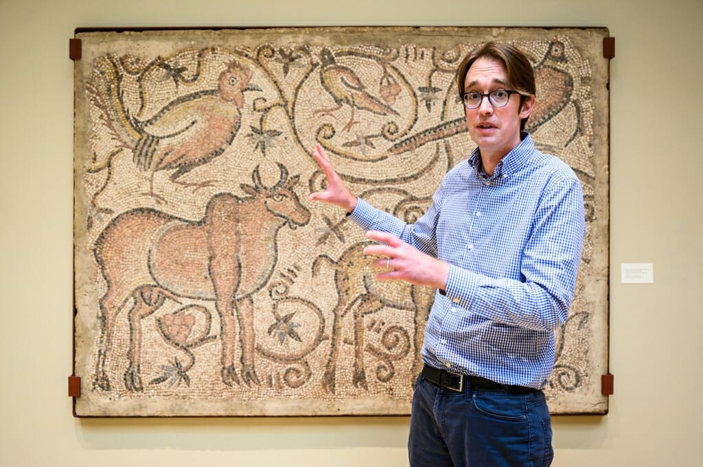 William Brockliss motioning toward a mosaic showing a bull and several birds